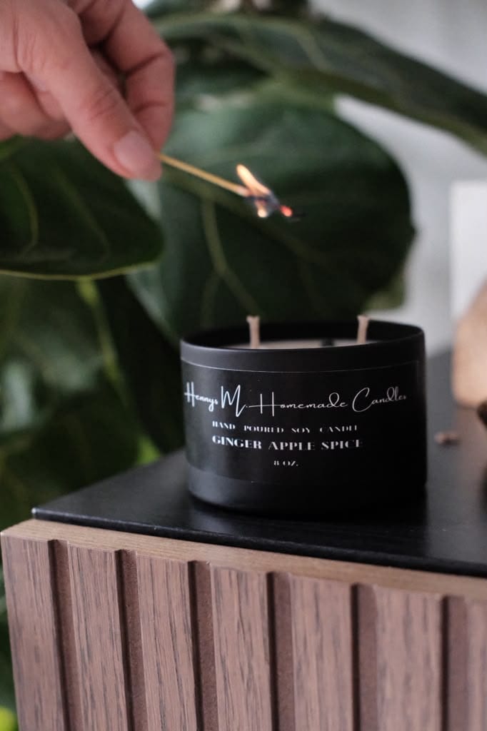 A match lit above the Ginger Apple Spice candle beside a large green leaf