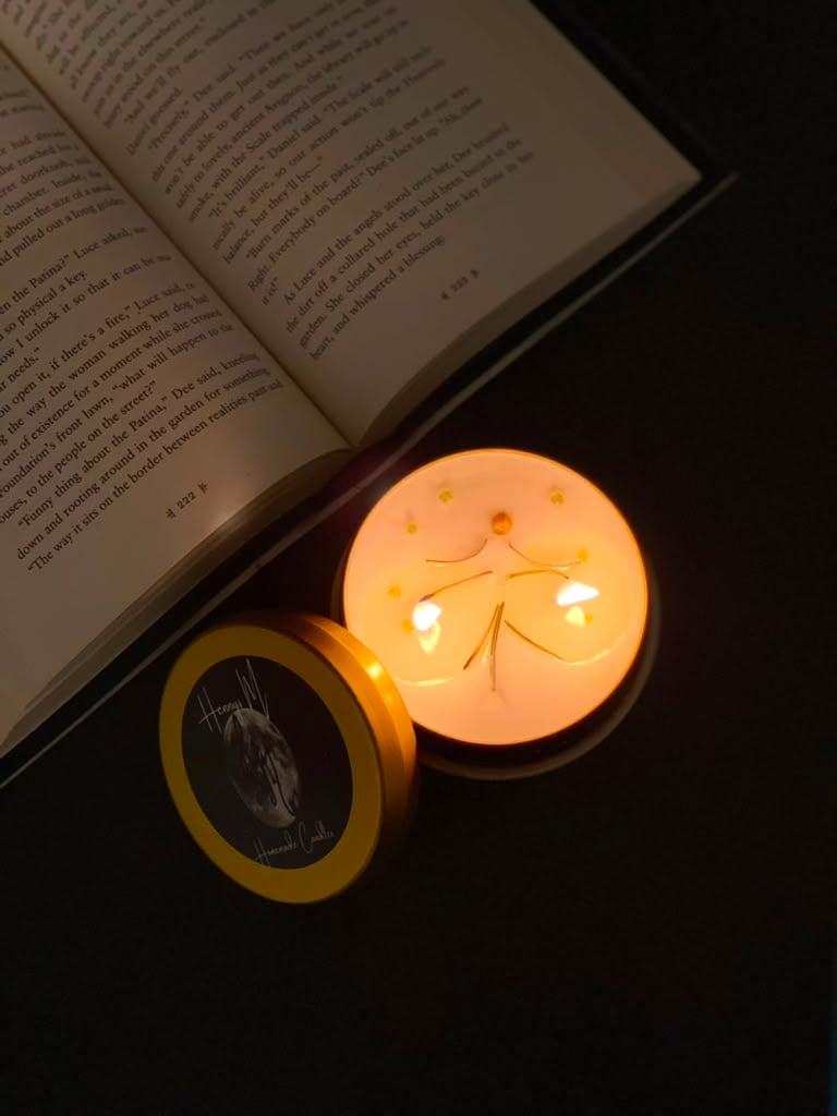 A gold Hennys M. candle burning beside an open book
